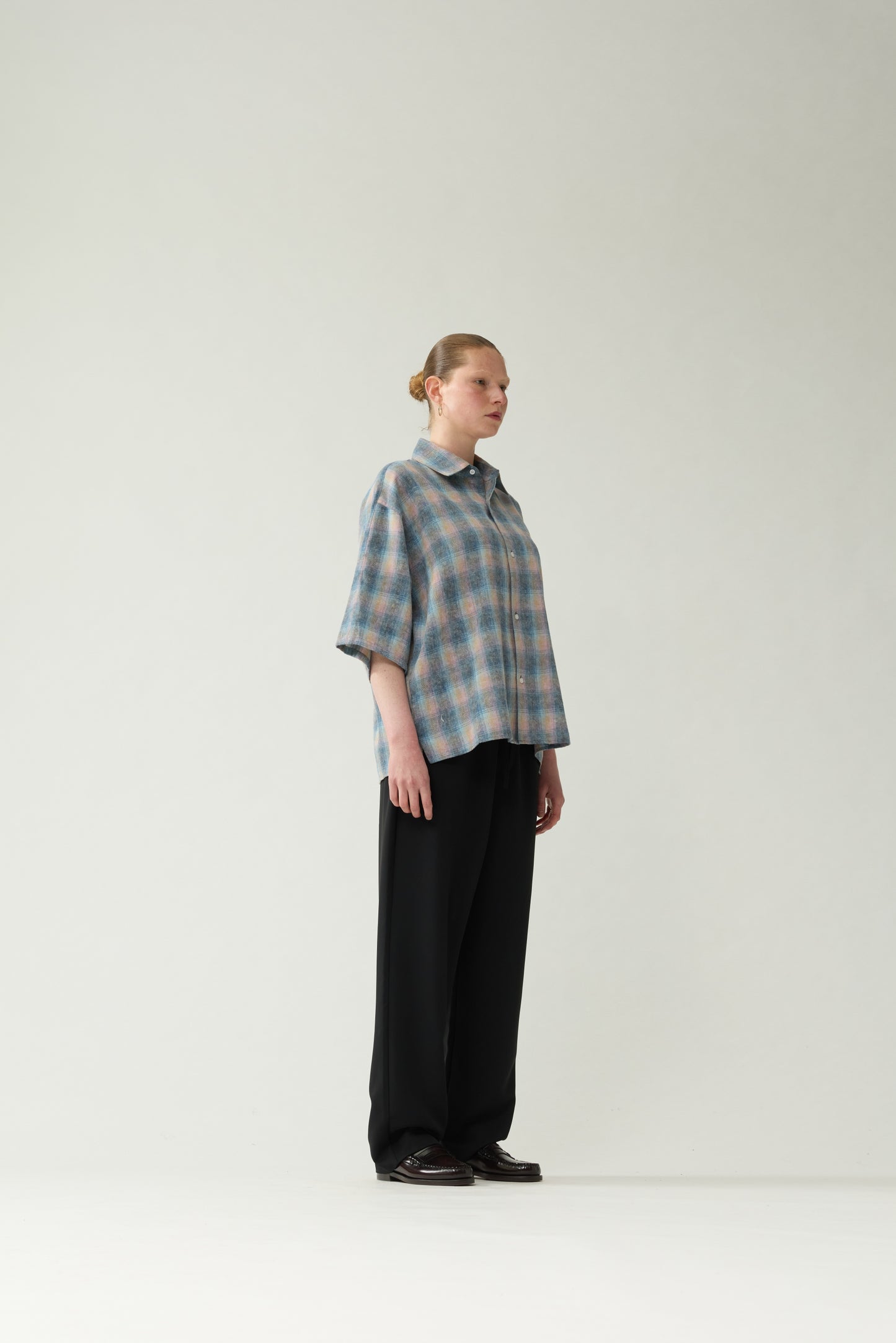 New Amsterdam Surf Association Flanel Short Sleeve Button-Up in Multicolour — female model wearing rainbow check flannel shirt, side view showing dropped shoulder silhouette and hip length