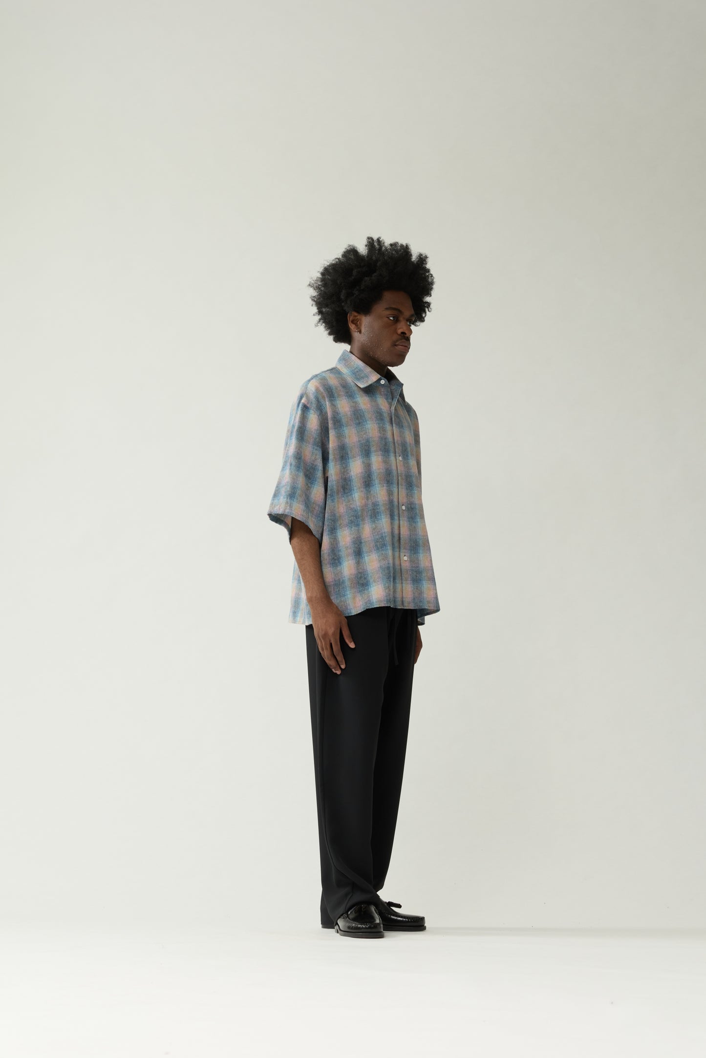 New Amsterdam Surf Association Flanel Short Sleeve Button-Up in Multicolour — male model wearing rainbow check flannel shirt, side view showing dropped shoulder silhouette and hip length