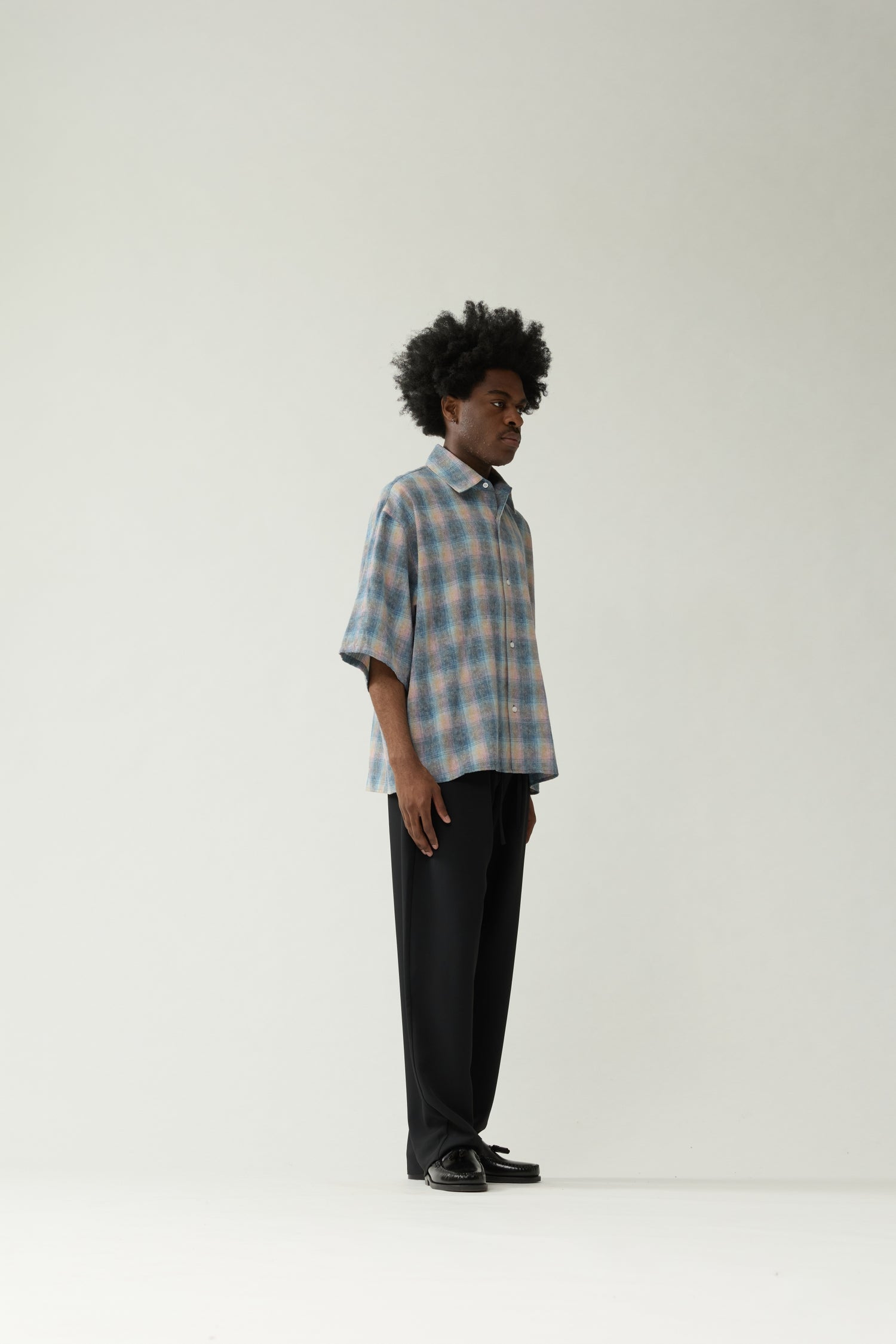 New Amsterdam Surf Association Flanel Short Sleeve Button-Up in Multicolour — male model wearing rainbow check flannel shirt, side view showing dropped shoulder silhouette and hip length
