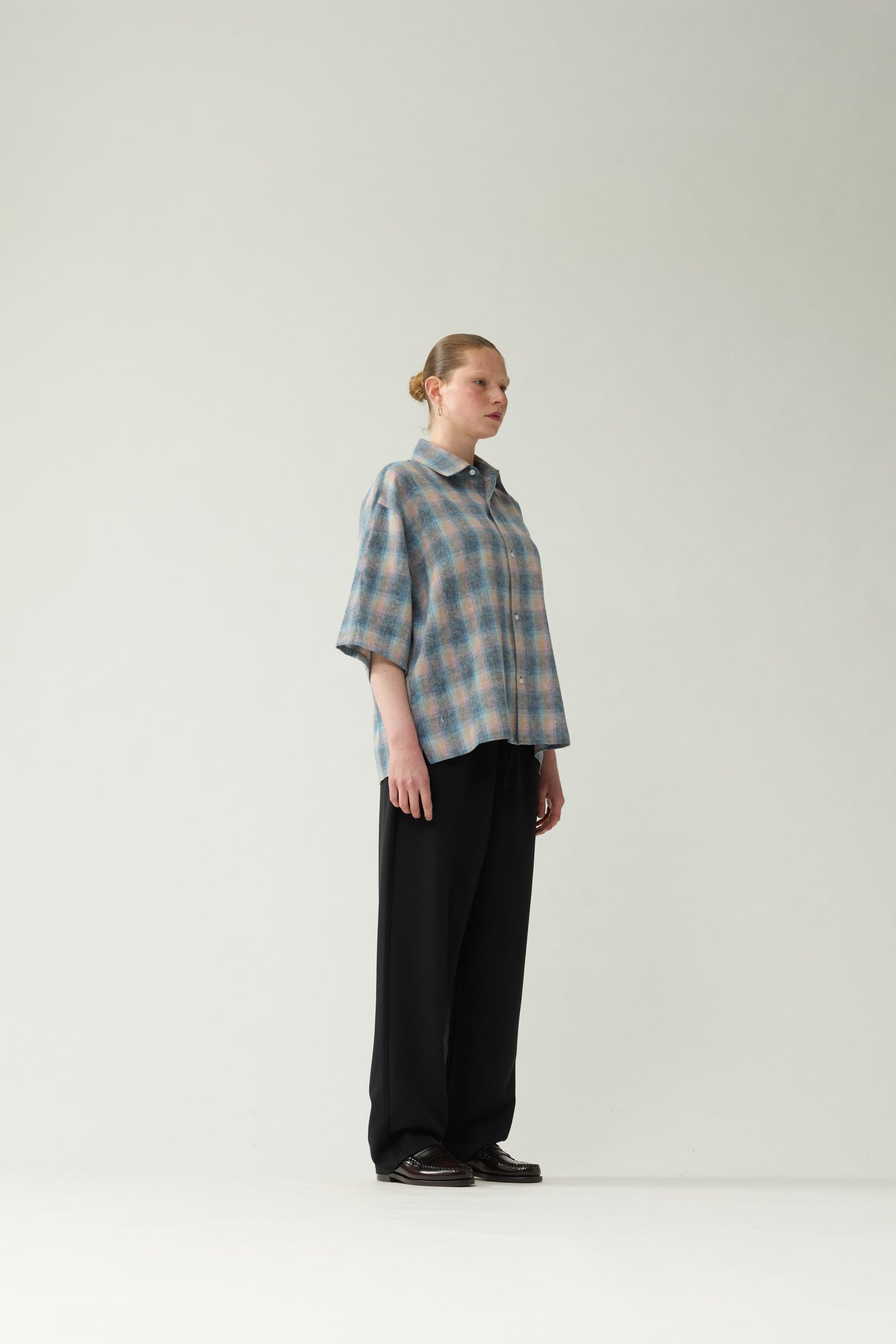 New Amsterdam Surf Association Flanel Short Sleeve Button-Up in Multicolour — female model wearing rainbow check flannel shirt, side view showing dropped shoulder silhouette and hip length