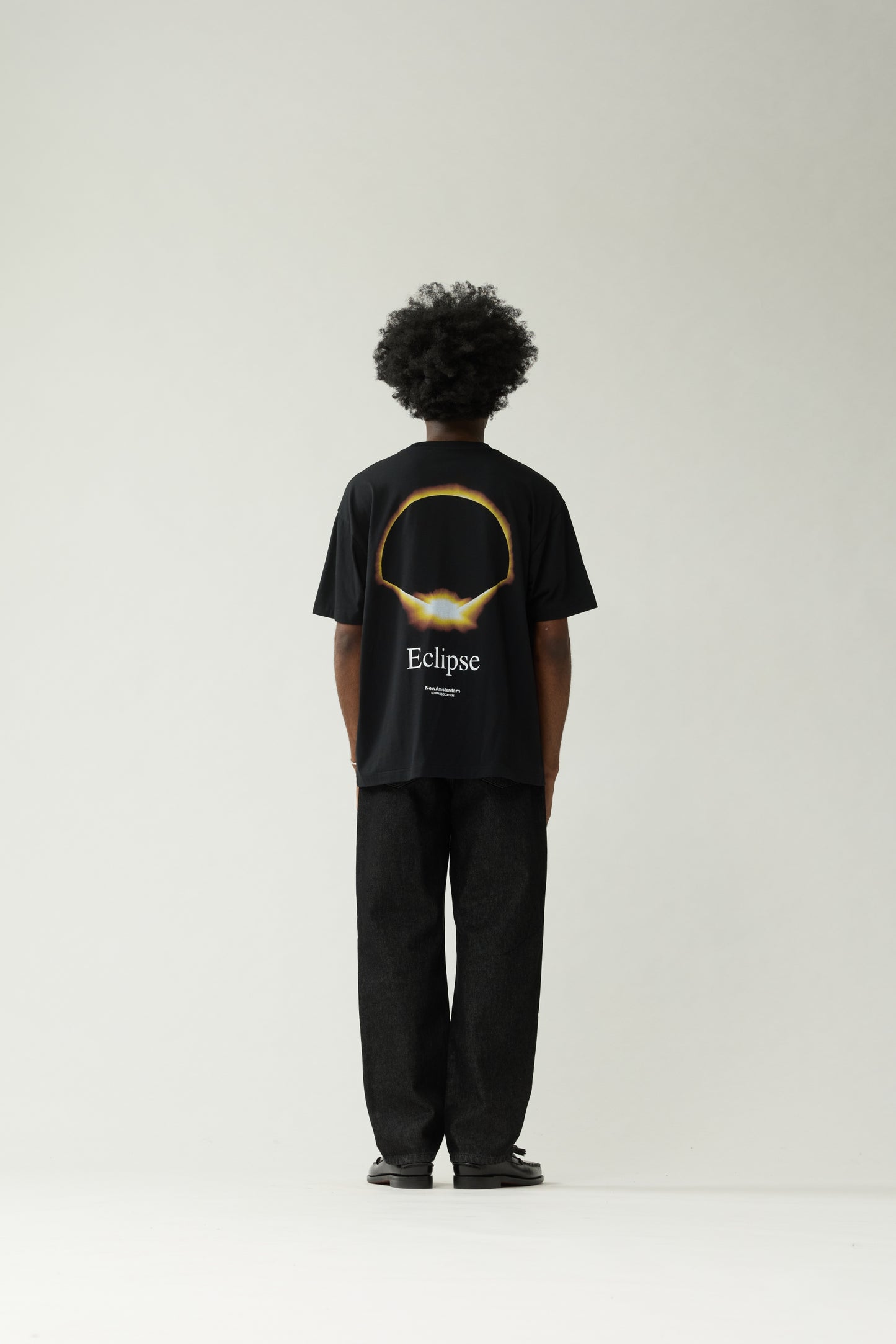 New Amsterdam Surf Association Black Eclipse Tee - Model Back View Full Body Golden Eclipse Ring Back Print T-Shirt