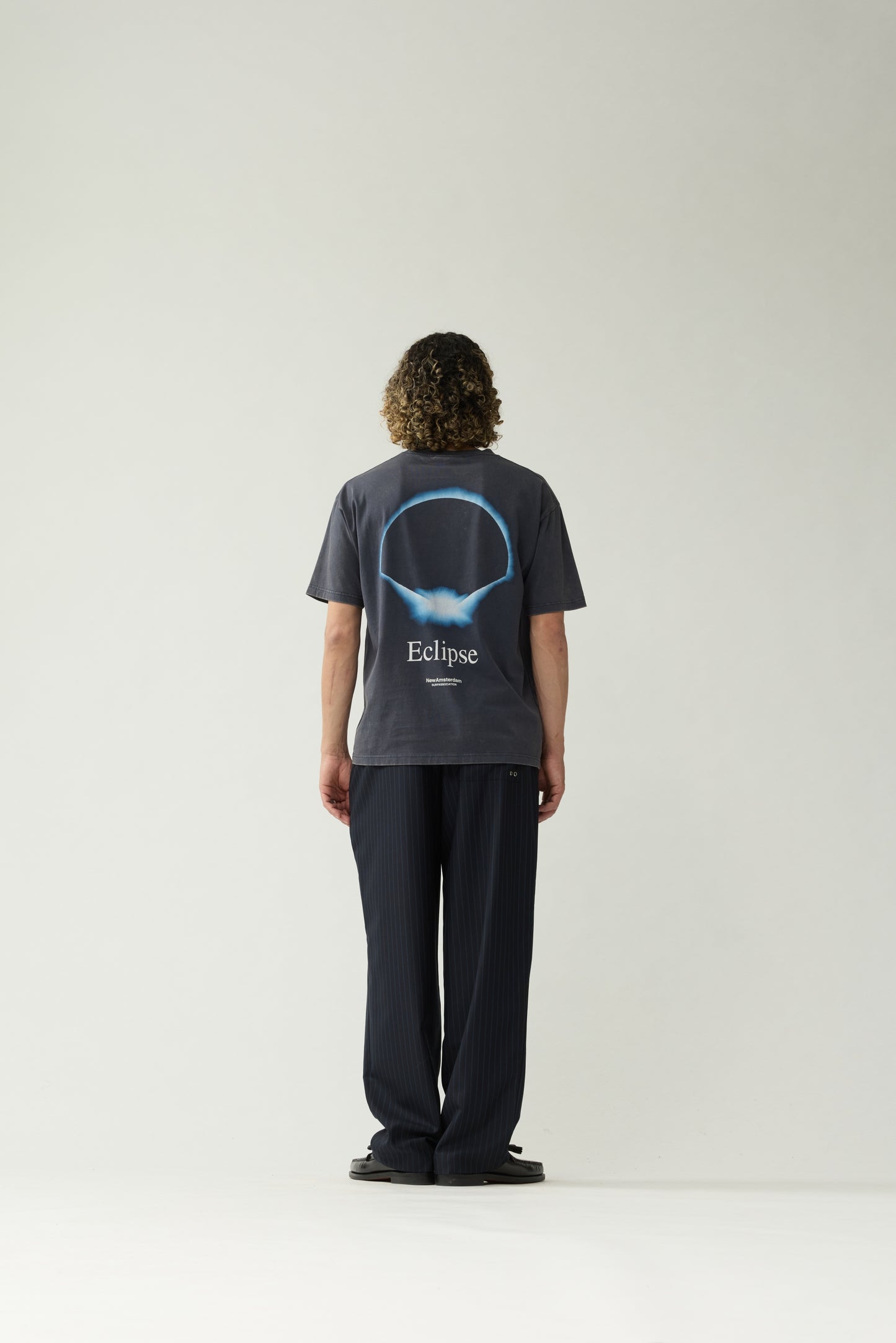 New Amsterdam Surf Association Eclipse Tee in Night — model wearing dark navy unisex crewneck tee, back view showing full Eclipse discharge print