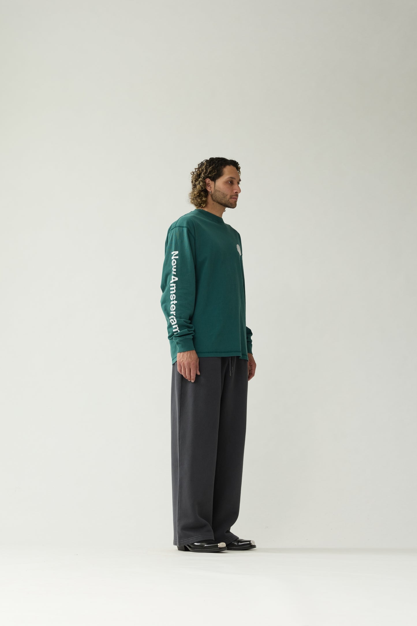 New Amsterdam Surf Association Logo Longsleeve in Bottle Green — male model wearing bottle green longsleeve, side view with "New Amsterdam" sleeve screenprint visible, regular fit