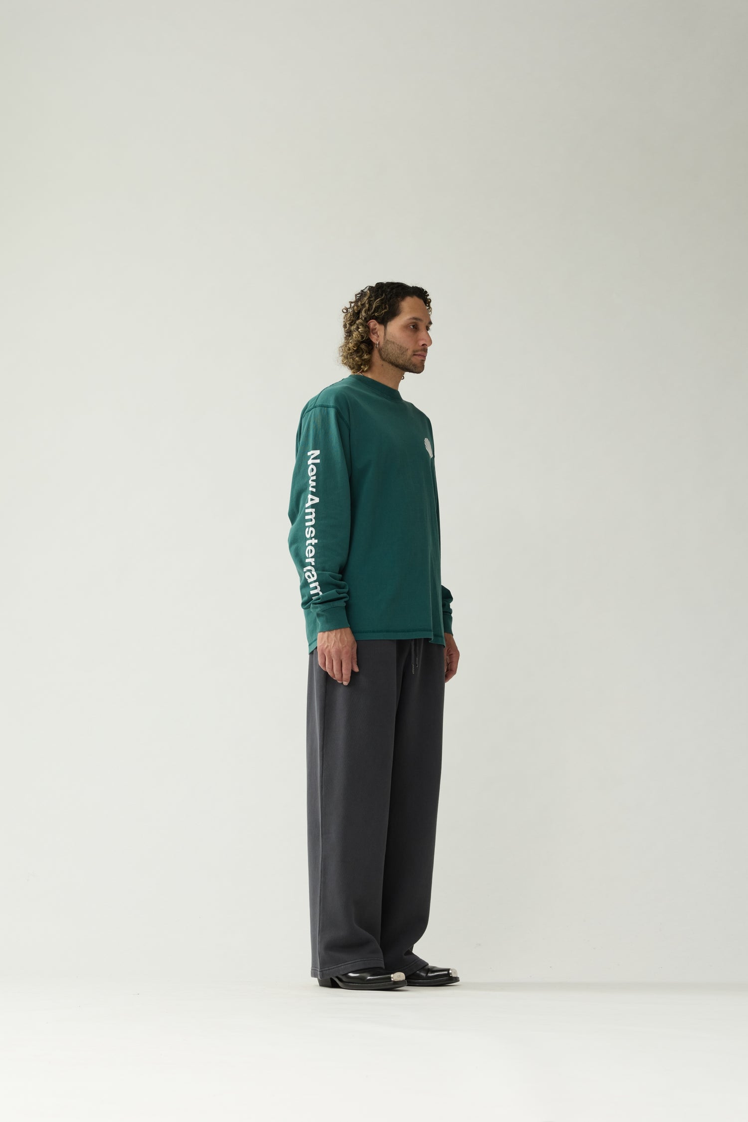 New Amsterdam Surf Association Logo Longsleeve in Bottle Green — male model wearing bottle green longsleeve, side view with "New Amsterdam" sleeve screenprint visible, regular fit