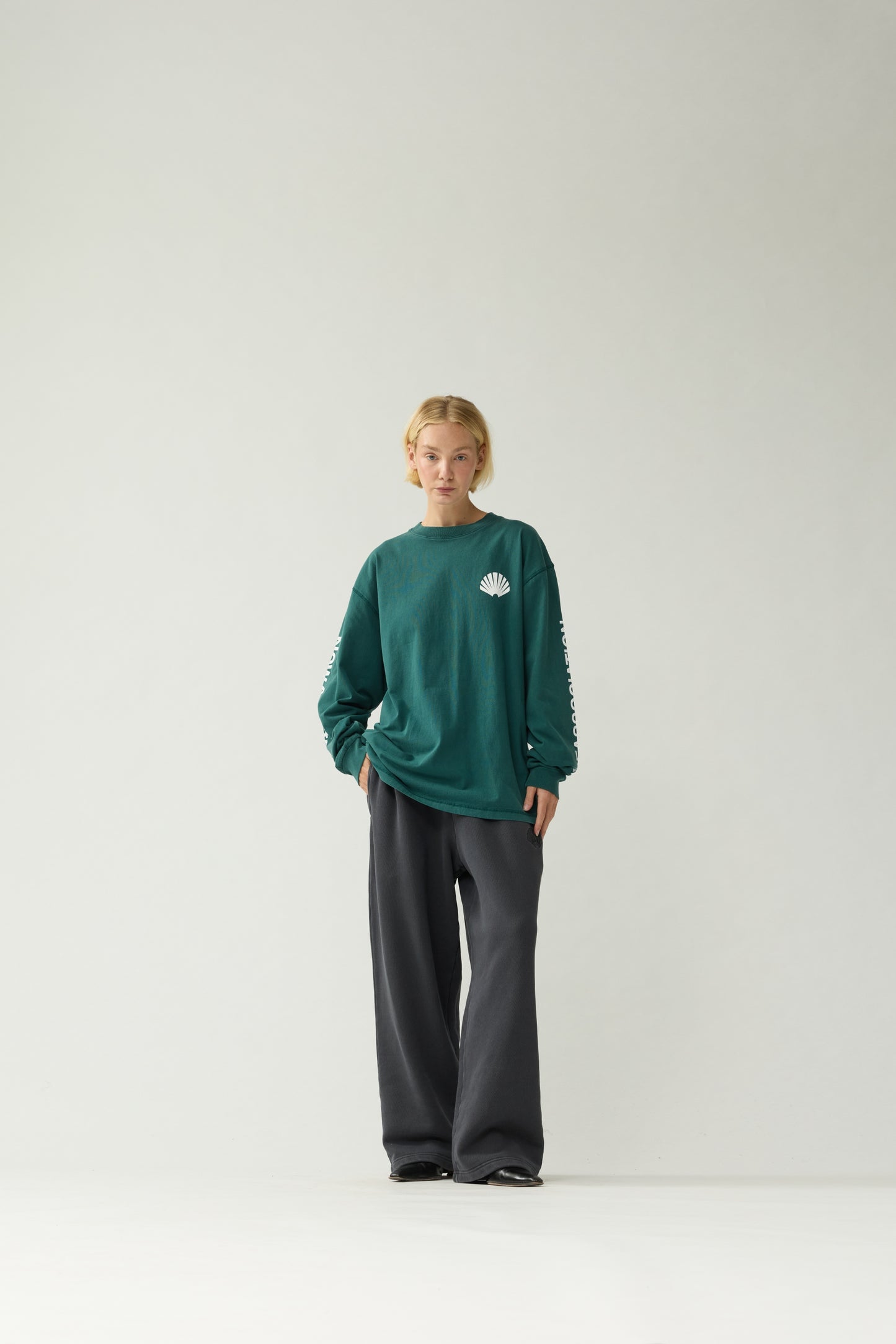 New Amsterdam Surf Association Logo Longsleeve in Bottle Green — female model wearing bottle green crewneck longsleeve, front view, regular unisex fit with shell logo on chest and sleeve screenprint
