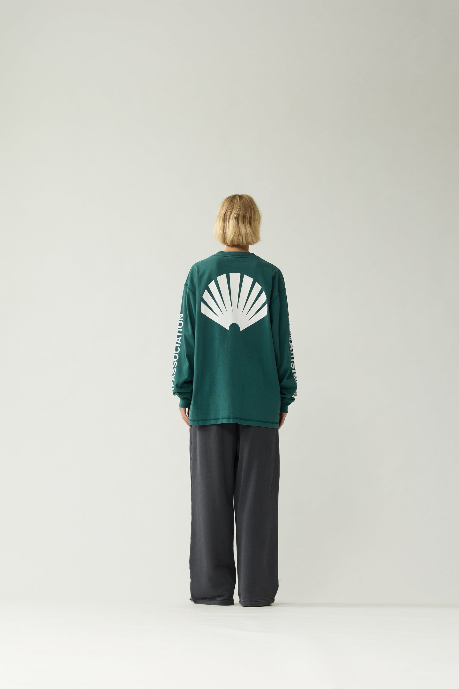 New Amsterdam Surf Association Logo Longsleeve in Bottle Green — female model wearing bottle green longsleeve, back view showing large white shell logo and "Surf Association" sleeve print