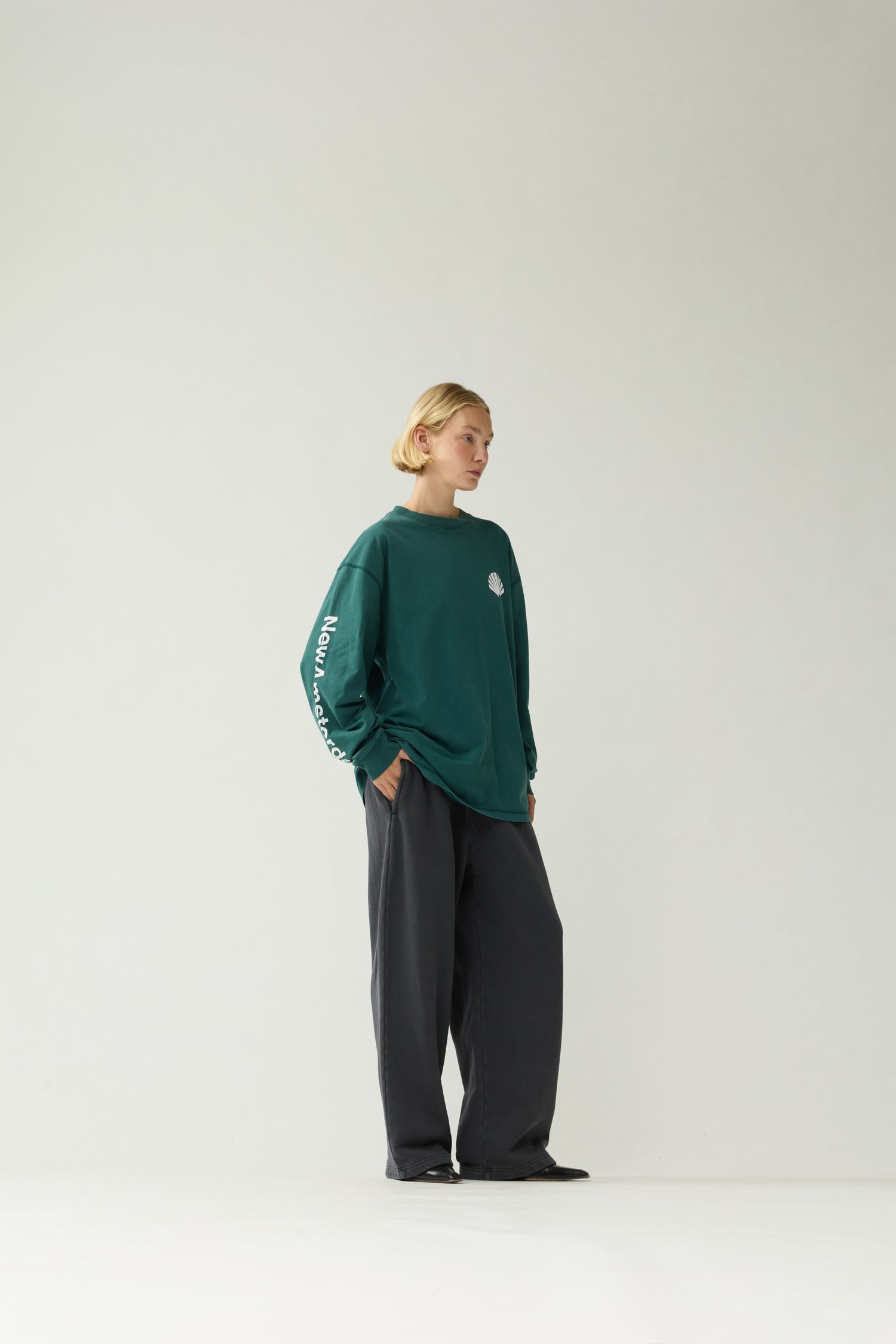 New Amsterdam Surf Association Logo Longsleeve in Bottle Green — female model wearing bottle green longsleeve, side view showing "New Amsterdam" sleeve screenprint and regular fit silhouette